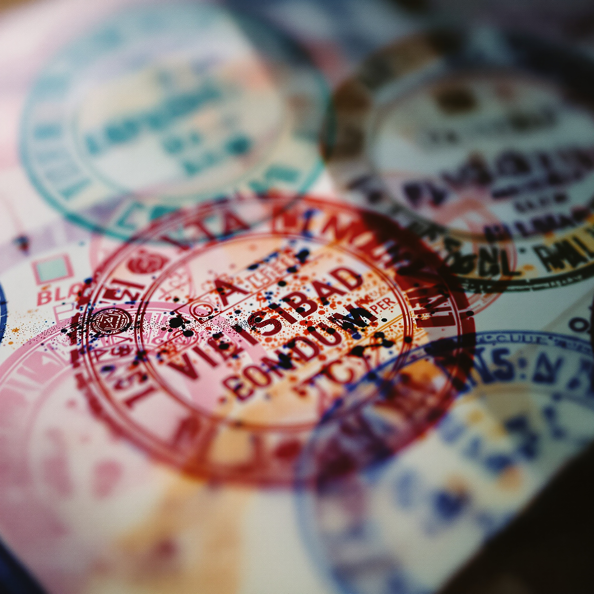 Macro photograph of colourful overlapping passport entry stamps in teal, red, pink and indigo
